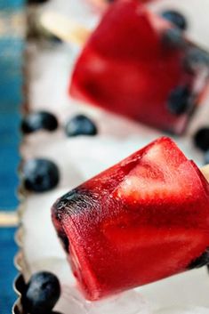 two popsicles with blueberries and strawberries on them sitting on ice cubes