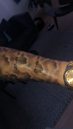 a person with tattoos on their arm has a watch on it's arm and is wearing a gold wristband