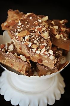 a white bowl filled with pieces of chocolate covered in nuts and caramel flakes