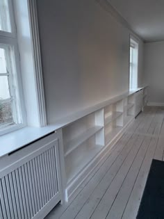 an empty room with bookshelves, radiator and window in the corner