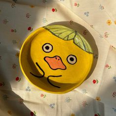 a yellow plate with a face painted on it sitting on a flowered tablecloth