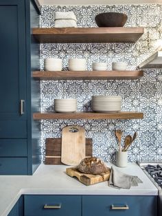 a kitchen with blue cabinets and open shelving above the stove top is filled with dishes