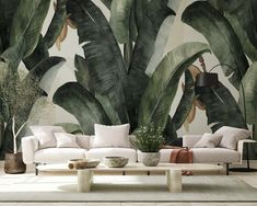 a living room with large green leaves on the wall and white couches in front of it