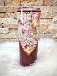 the tumbler cup is decorated with flowers and hearts on it's side, sitting on a fluffy white surface