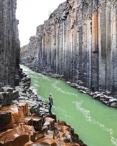 a man standing on the edge of a cliff next to a river with green water