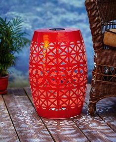 a red vase sitting on top of a wooden table next to a wicker chair