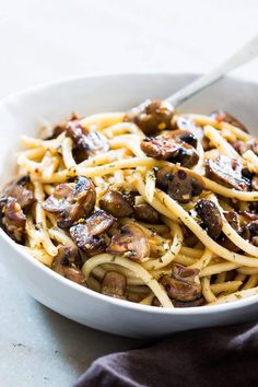 a white bowl filled with pasta and mushrooms on top of a table next to a fork