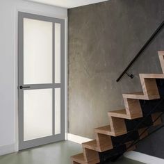 an open door leading to a stairway with wooden steps and railings in front of a gray wall