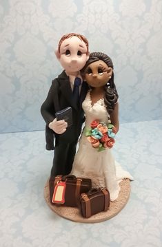 a wedding cake topper with a bride and groom holding suitcases on a table