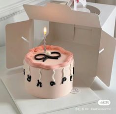 a birthday cake with a lit candle on it in front of an open cardboard box