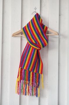 a multicolored scarf hanging from a wooden hanger on a white wall with wood slats