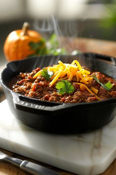 a skillet filled with chili and cheese on top of a cutting board