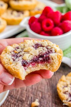 a hand holding a berry crumb cookie over a table full of raspberries