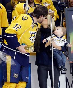 a man kissing a woman while holding a baby in front of an ice hockey rink