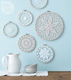 there are four white doily hanging on the wall next to a pitcher and stack of plates