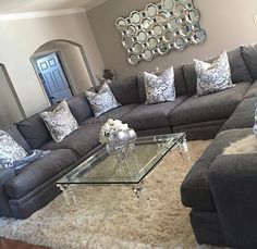 a living room with grey couches and mirrored coffee table in front of a mirror on the wall