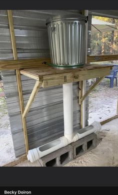 a metal bucket sitting on top of a wooden shelf next to a white pipe under a roof