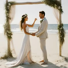 a bride and groom standing under an arch on the beach with their hands in each other's pockets