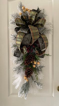 a christmas wreath hanging on the front door with pine cones and evergreens attached to it