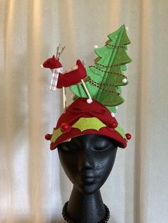 Cuter than cute. Original scene tops off this vintage hat. Red wool fitted hat with black elastic strap to hold hat in place. A tall 4 sided felt tree with red garland stands opposite two felt deer (red and white)with thin wood legs. Small white puff balls represent snowflakes gently falling. The rim of the hat is trimmed with felt holly leaves and red berries. A small red bow finishes off the rim of the hat hat which can be worn either direction. Unique creation, made in Iowa by Red Button Art Scene Tops, Felt Holly, Felt Deer, Puff Balls, Red Garland, Felt Tree, Holly Leaves, Vintage Hat, Button Art