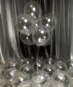 several clear balloons are floating in the air near silver curtained drapes and sheer curtains