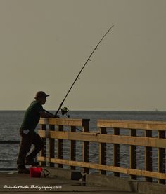 a man is fishing on the pier by the water