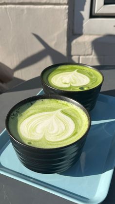 two black bowls filled with green liquid on top of a blue tray