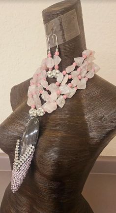 Soft baby pink rough dusty rose quartz gemstones along with sculpted pink rhinestone balls are featured in this one-of-a-kind multi strand statement necklace pendant - chest piece. This avant garde piece would be gorgeous worn on the mother of the bride or mother of the groom. The prehistoric black and white fossil pendant measures 7" x 2.25" and is bejeweled with extra large silver tone rhinestones and soft baby pink Swarovski crystals (I will send additional pink crystals in the event some should fall off). Two 1" silver tone rhinestone balls flank each side of the pendant. The rough quartz necklace adjusts from 16-19" and is finished in the back with pink aurora borealis crystals cubes. It closes with silver tone hardware, a fancy "s" hook clasp and a 4" extender chain. A rhinestone bal Pink Rose Quartz Jewelry For Party, Pink Rose Quartz Jewelry With Stones, Pink Rose Quartz Party Jewelry, Rose Quartz Jewelry With Natural Stones For Wedding, Handmade Pink Crystal Jewelry, Pink Kunzite Jewelry For Wedding, Unique Pink Jewelry With Stones, Pink Crystal Jewelry With Stones, Pink Rose Quartz Wedding Jewelry