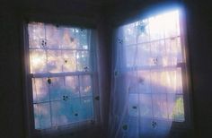 two windows with white curtains and the sun shining through them, in a dark room