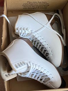 two pairs of white tennis shoes in a box with laces on the soles