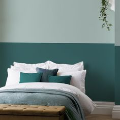 a bed with white and green pillows in a bedroom next to a plant hanging on the wall