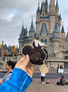 a person holding up a mickey mouse pin in front of a castle with people sitting on the ground