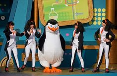 the penguins are singing on stage with one penguin in front of them and four other people standing around