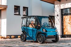 a blue electric golf cart parked in front of a white building with two people inside