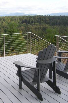 two adiron chairs sitting on top of a wooden deck next to a forest filled with trees