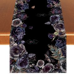 a black table runner with purple flowers and leaves on the edge, along with a wooden table