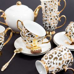 a table topped with cups and saucers covered in leopard print on white plates next to gold trimmings