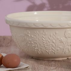 an egg sits next to a white bowl with flowers on it and two brown eggs