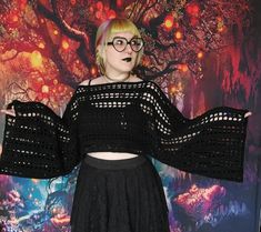 a woman wearing glasses and a black crochet top stands in front of a colorful background