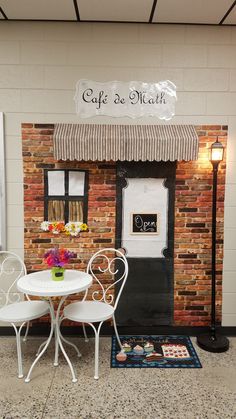 two white chairs and a table in front of a building with a sign that says cafe de math