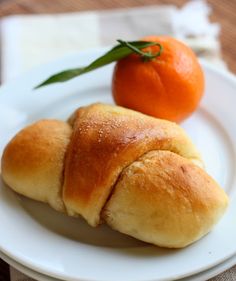 two croissants on a plate next to an orange