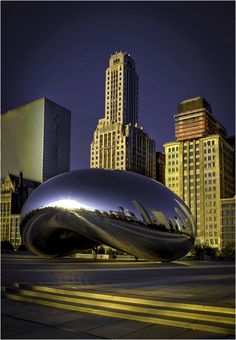 an artistic sculpture in the middle of a city with tall buildings behind it at night