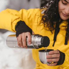 a woman pouring water into a cup in the snow