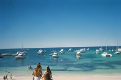 two women walking on the beach with boats in the water