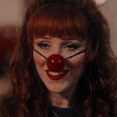 a woman with long red hair wearing a clown nose