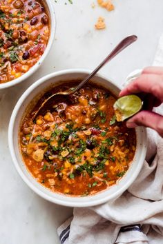 two bowls of chili and beans soup with a spoon in one bowl the other is being held up by someone's hand