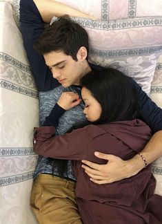 a man and woman laying on top of a bed next to each other with their arms around each other