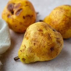 three yellow pears sitting next to each other on a white counter top with brown spots