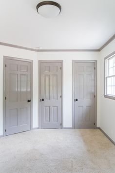 an empty room with three white doors and two windows in the corner, all painted gray