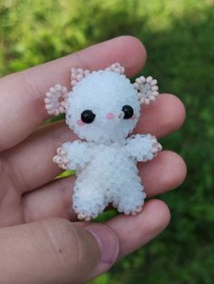 a small white stuffed animal sitting on top of a persons hand in front of some grass